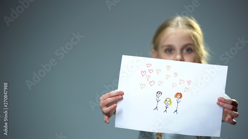 Cheerful little girl showing family picture into camera, feeling parental love photo