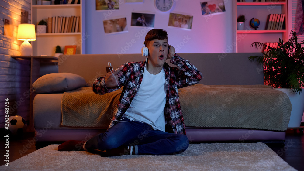 Obraz premium Excited teenager in headphones listening to favourite music sitting in his room
