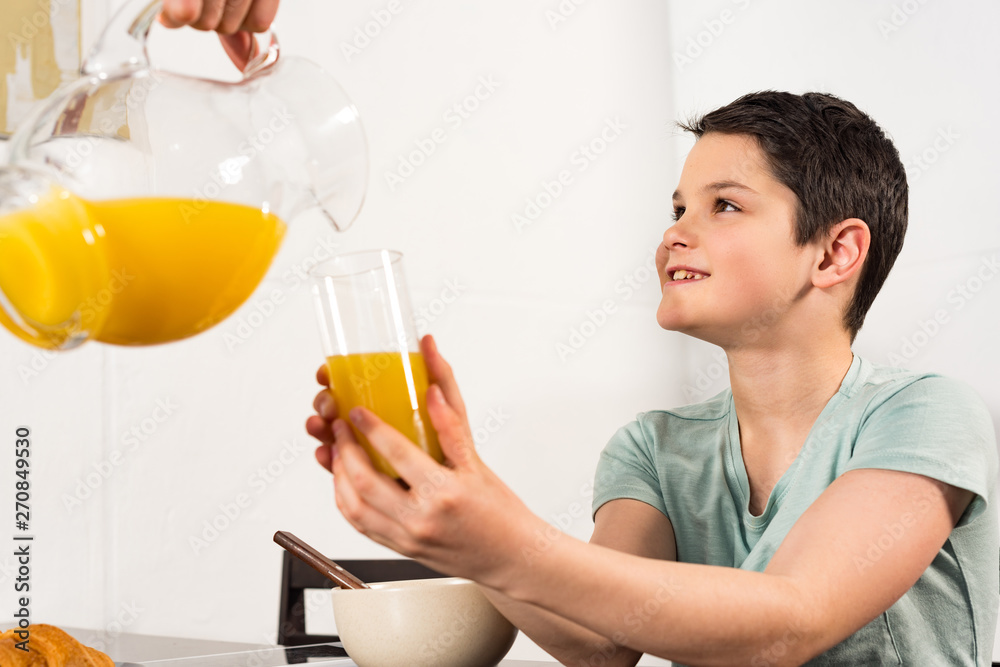 cropped view of father pouring orange juice to son in kitchen cropped view of father pouring orange juice to son in kitchen