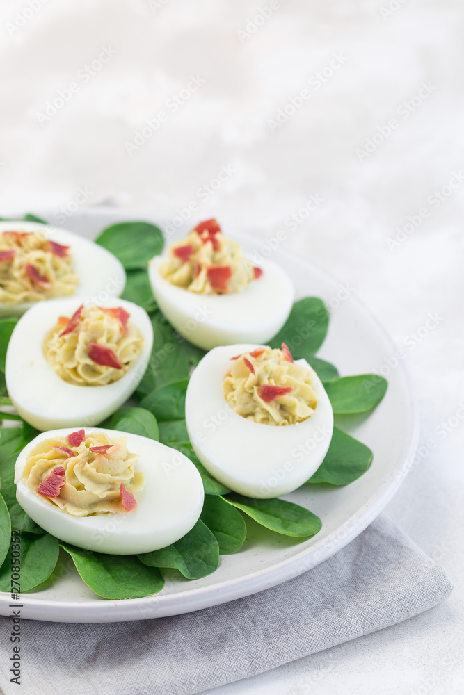Deviled eggs stuffed with avocado, egg yolk and mayonnaise filling, garnished with bacon, on spinach leaves, vertical copy space