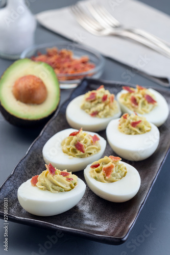 Deviled eggs stuffed with avocado, egg yolk and mayonnaise filling garnished with bacon, vertical