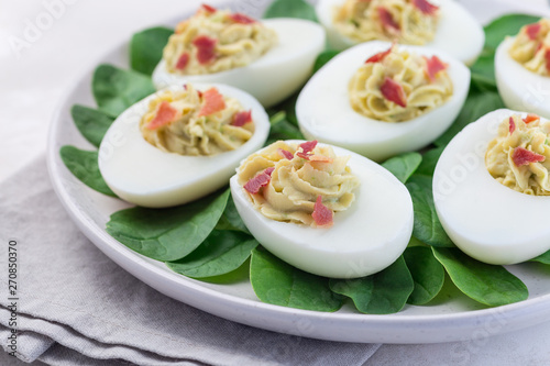 Deviled eggs stuffed with avocado, egg yolk and mayonnaise filling, garnished with bacon on spinach leaves, horizontal