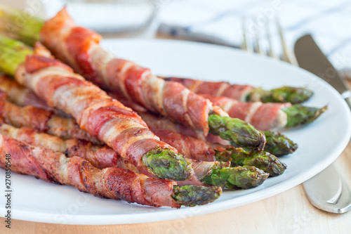 Green asparagus wrapped with bacon on white plate, horizontal