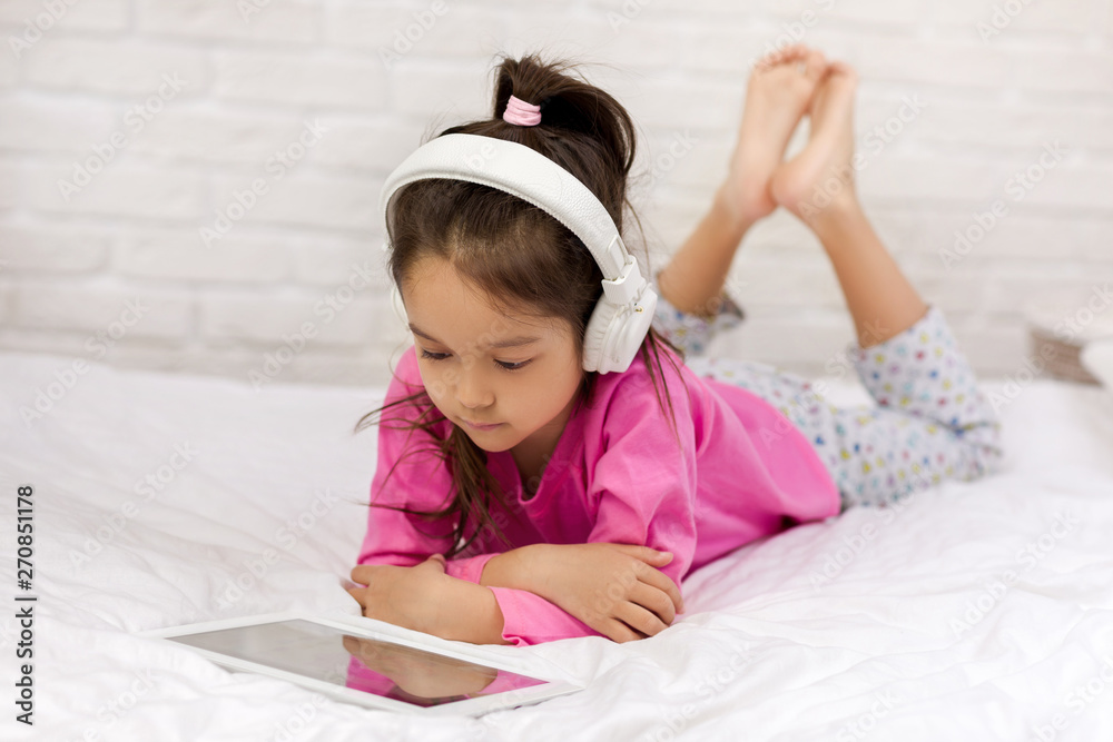 cute little child girl lies in bed uses digital tablet. child playing on tablet pc. cute little child girl lies in bed uses digital tablet. child playing on tablet pc.
