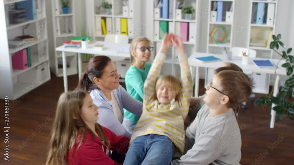 High-angle shot of smiling blond teenage boy slowly falling backwards and other kids with female teacher catching him, while standing in pairs and gripping each other’s hands High-angle shot of smiling blond teenage boy slowly falling backwards and other kids with female teacher catching him, while standing in pairs and gripping each other’s hands