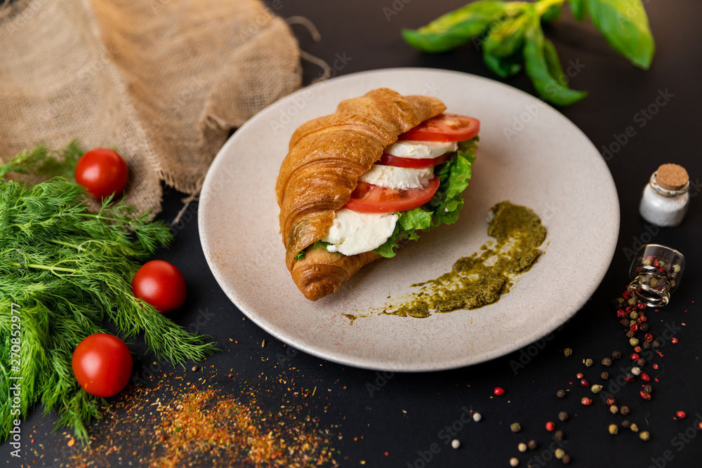 Breakfast croissant sandwich with mozzarella and tomatoes. Top view. black background with vegetables. Slow-mo.