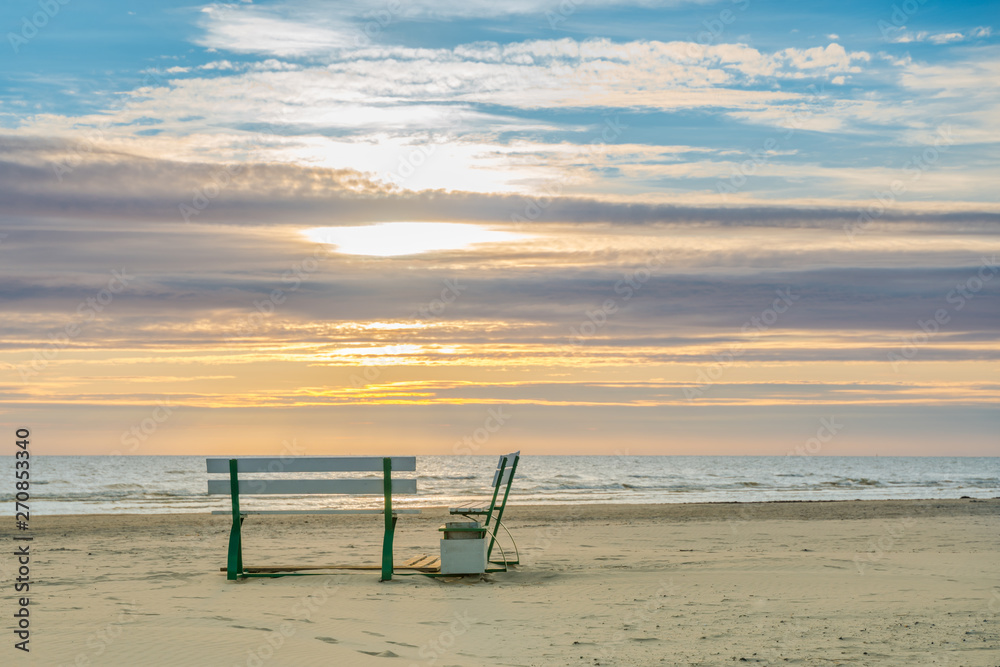  Very beautiful sunset on the sea and a place to relax on the shore near the water. Two benches on the sandy seashore.