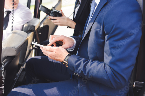 cropped view of businessman in formal wear sitting in helicopter with smartphone