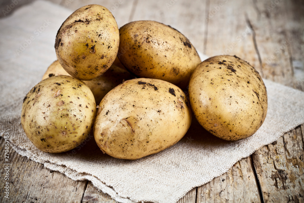 Fresh organic dirty potatoes heap closeup on linen tablecloth on rustic wooden background. Fresh organic dirty potatoes heap closeup on linen tablecloth on rustic wooden background.