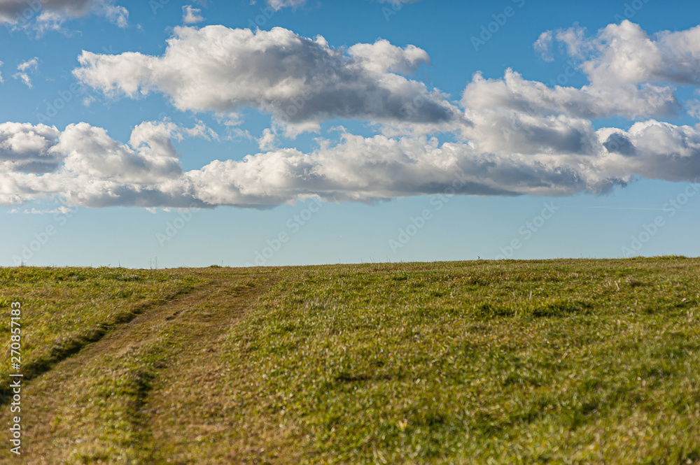 Faint tracks going up a grass hill. Cloudy but sunny sky. Faint tracks going up a grass hill. Cloudy but sunny sky.