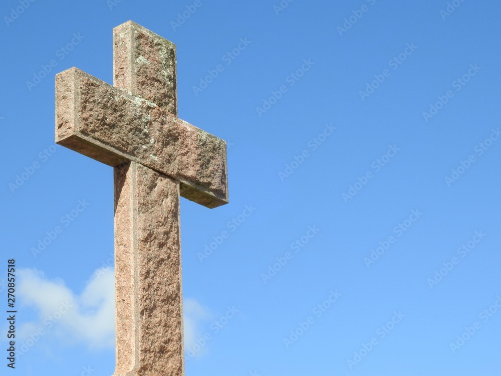 Scene in a graveyard: close-up of a religious stone cross illuminated by the sun. Blue sky on a sunny day. Faith and religiosity.