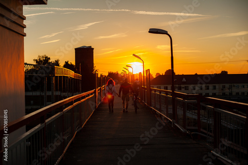 Family with a bicycle go on the bridge against the setting sun