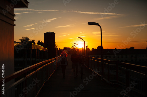 Family with a bicycle go on the bridge against the setting sun