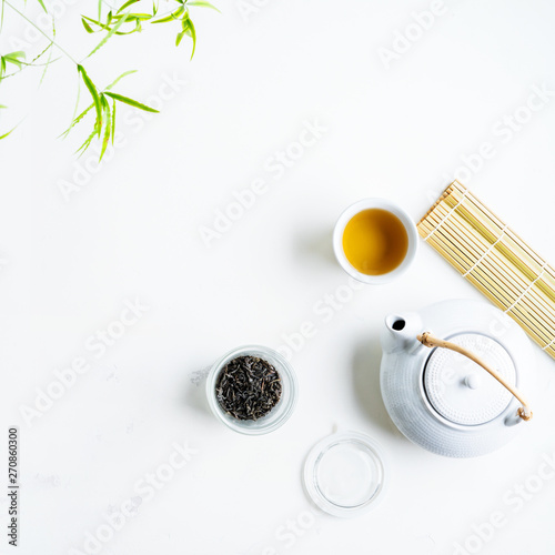 Asian tea concept, two white cups of tea and teapot surrounded with green tea dry leaves , space for a text on white background. Brewing and Drinking tea.