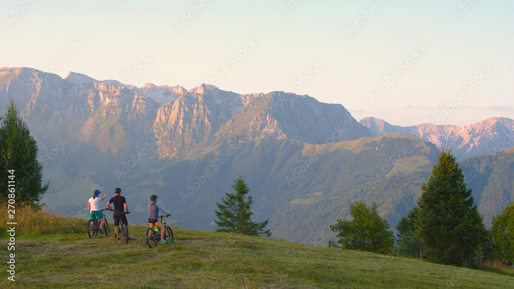 COPY SPACE: Three friends on mountain bikes observe the scenic sunlit mountains.