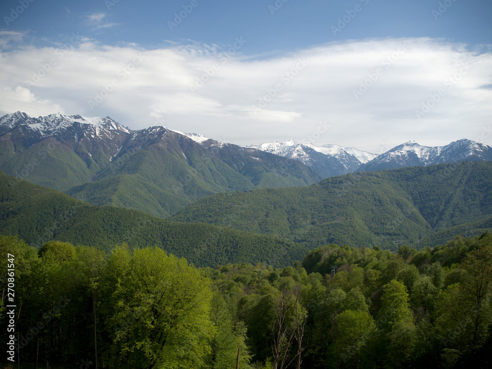 Beautiful green mountains below and mountains with snow at the height of Krasnaya Polyana