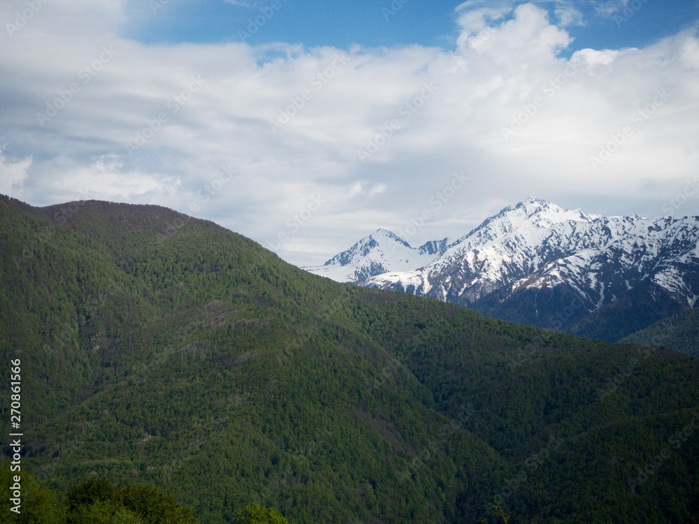 Beautiful green mountains below and mountains with snow at the height of Krasnaya Polyana