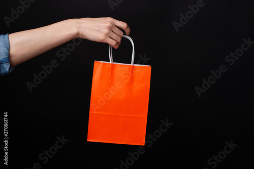 Картината върху платно Woman hand holding orange shopping bag over black background