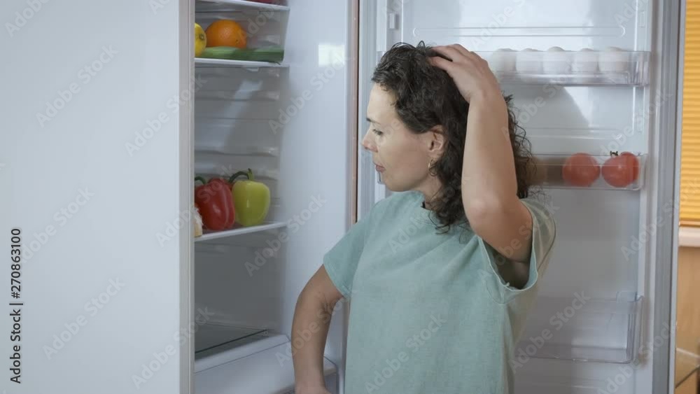 Woman open the refrigerator for food. Thoughtful woman looks into the refrigerator. Woman open the refrigerator for food. Thoughtful woman looks into the refrigerator.