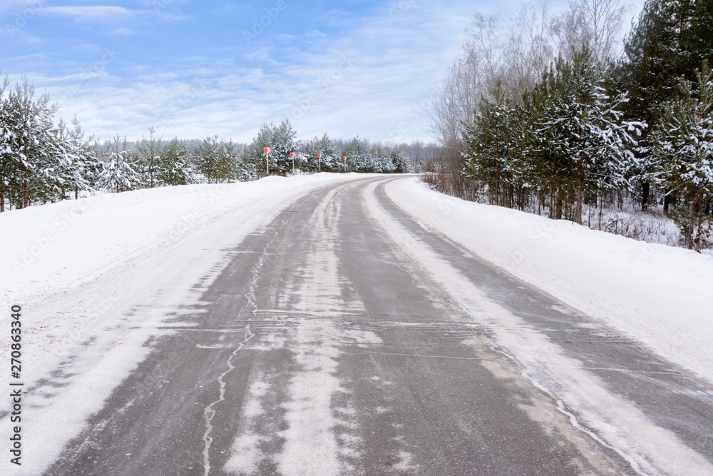 Patterns on the winter highway in the form of four straight lines. Snowy road on the background of snow-covered forest. Winter landscape. Patterns on the winter highway in the form of four straight lines. Snowy road on the background of snow-covered forest. Winter landscape.