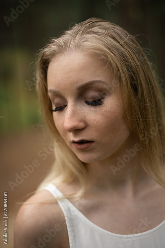 Close up portrait - Beautiful young blonde woman forest nymph in white dress in evergreen wood