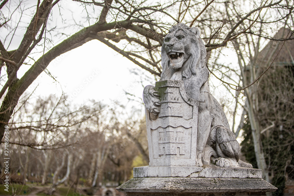 Lion stone statue is among the trees at the park at Budapest