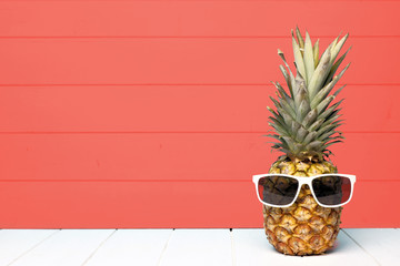 Hipster pineapple with sunglasses against a living coral colored wood background. Minimal summer concept.
