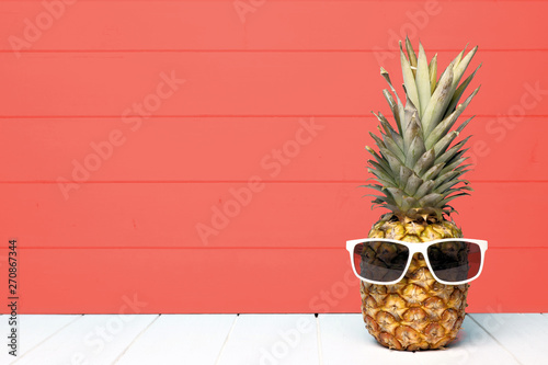 Hipster pineapple with sunglasses against a living coral colored wood background. Minimal summer concept.