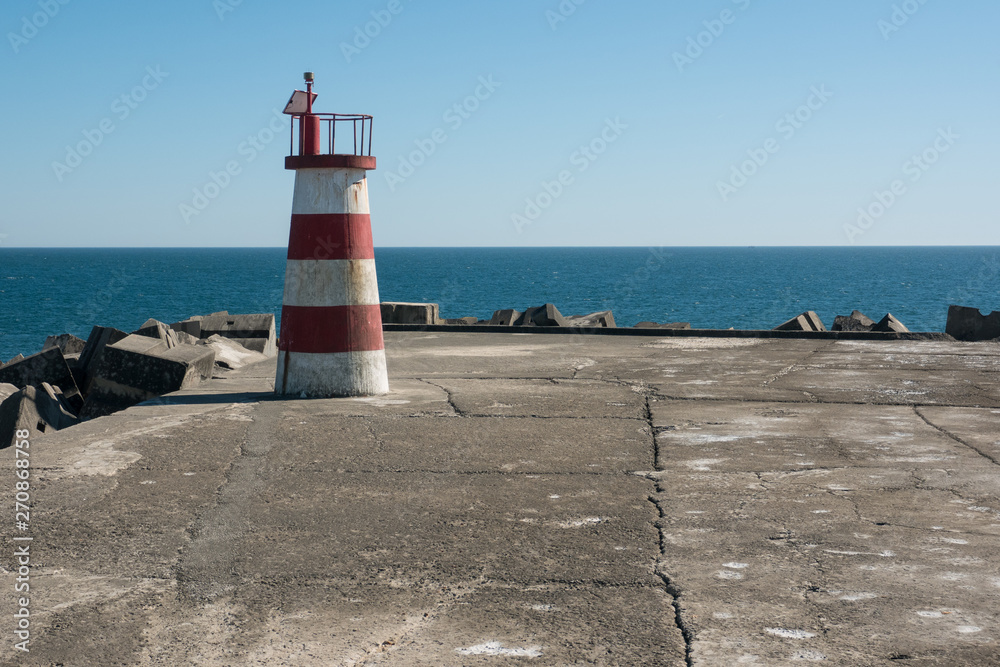 Red and white light house at end of harbour wall in Povoa de Varzim, Portugal, with ocean in background