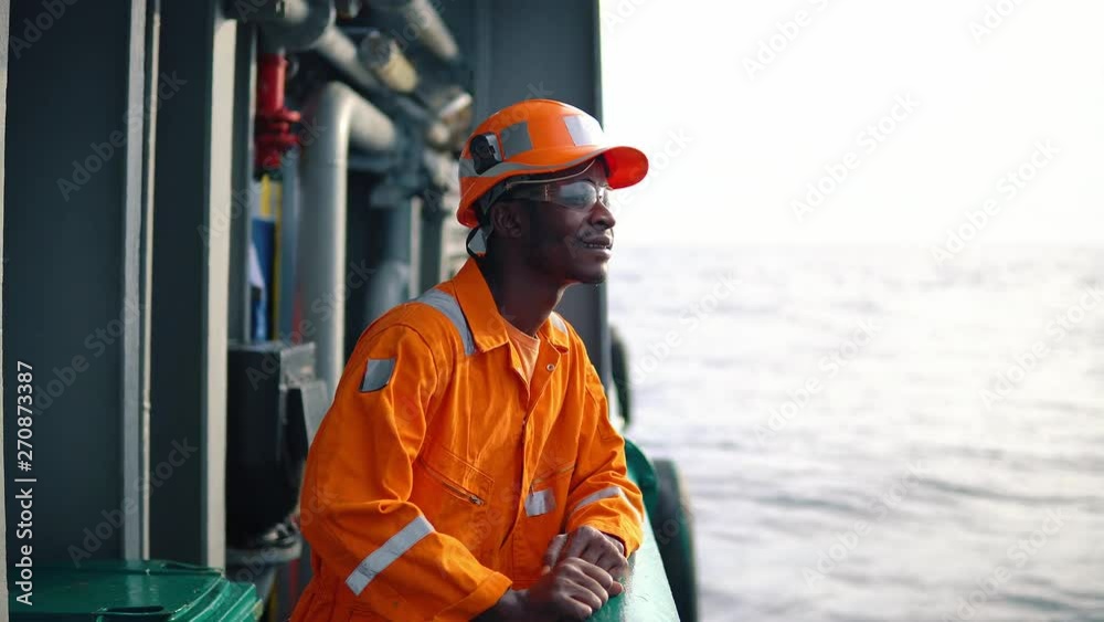 Tired Seaman AB or Bosun on deck of vessel or ship , wearing PPE personal protective equipment - helmet, coverall, lifejacket, goggles. Safety at sea Tired Seaman AB or Bosun on deck of vessel or ship , wearing PPE personal protective equipment - helmet, coverall, lifejacket, goggles. Safety at sea