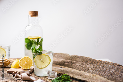 Bottle and two glasses of fresh lemonade with lemon slices, mint and ice on old wooden planks. Copy space