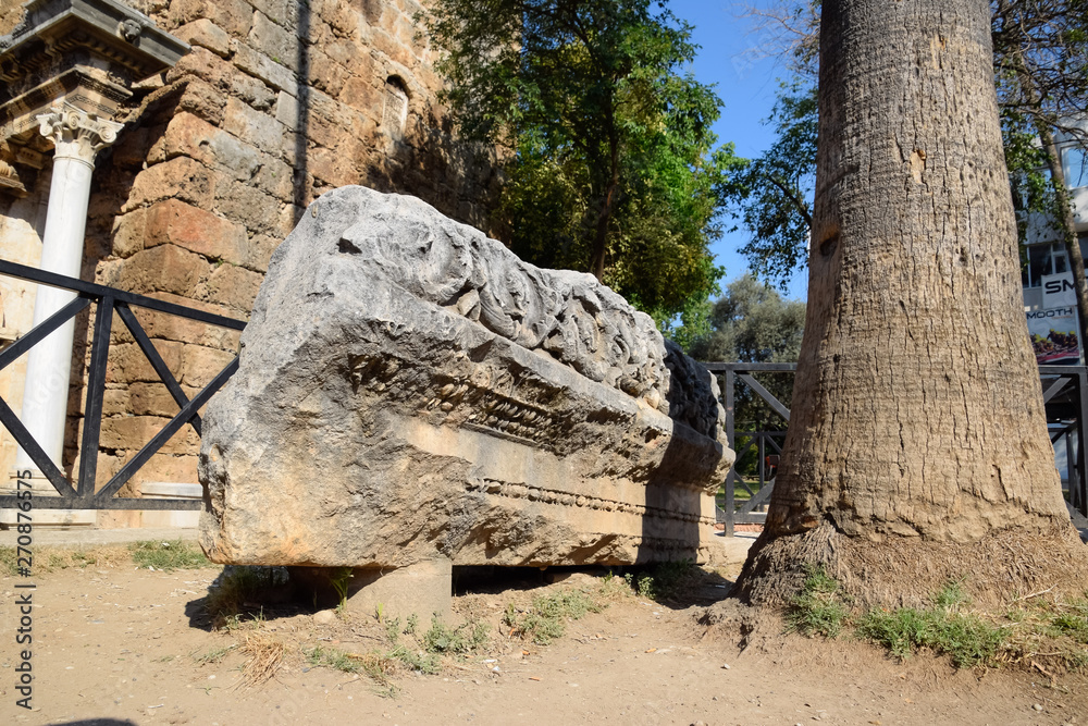 Obraz premium The element of the gate of Hadrian on the ground near the gate. Ruins of ancient construction.