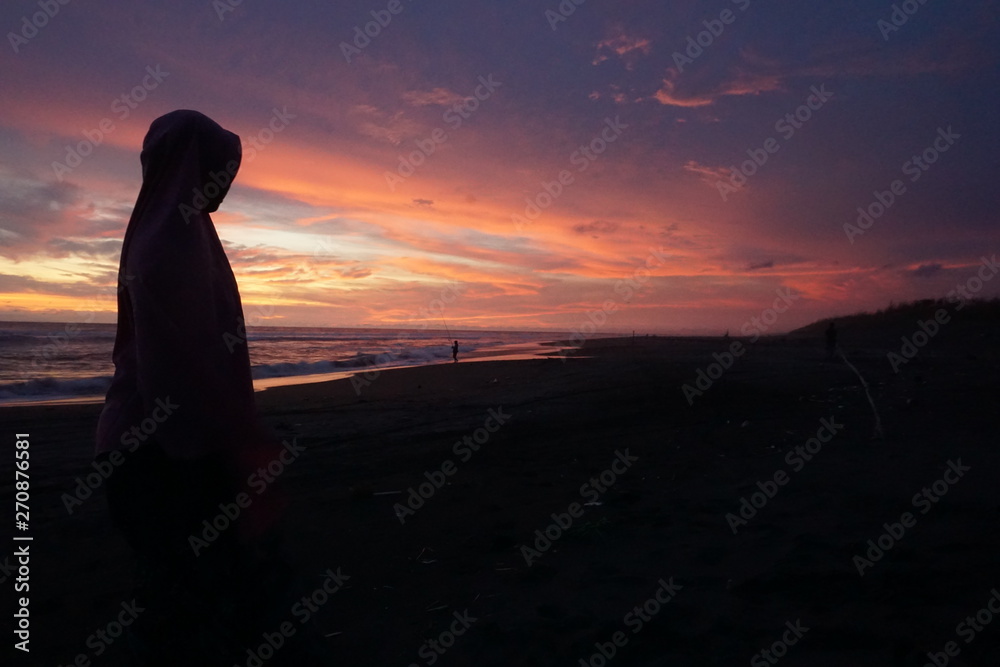the sun rises during the summer on the beach with the foreground of the silhoutte Muslim women wearing hijab