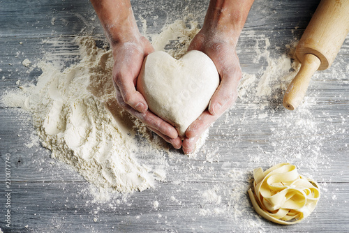 Heart shaped dough held by baker's hands in close-up.