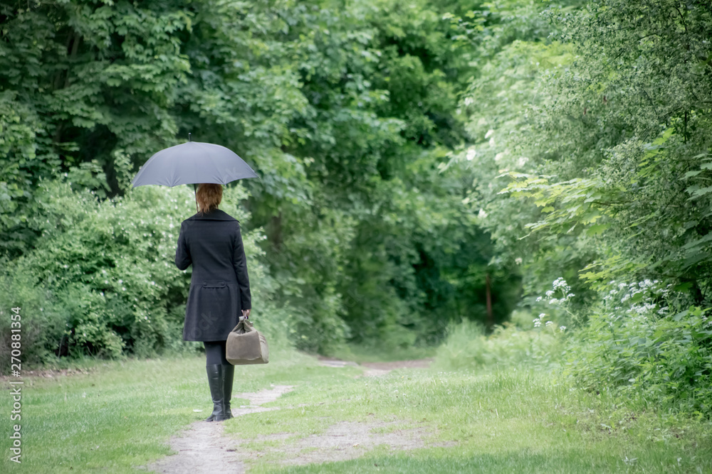 A lonely woman goes with umbrella and travel bag along a forest road. Concept loneliness.