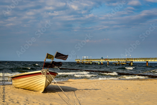 Boot mit im Wind flatternden Wimpeln am Strand von Usedom. Im Hintergrund die Seebr  cke von Koserow
