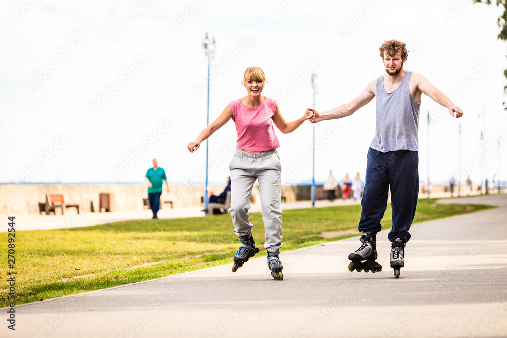 Young couple rollerblading in park holding hands. Young couple rollerblading in park holding hands.