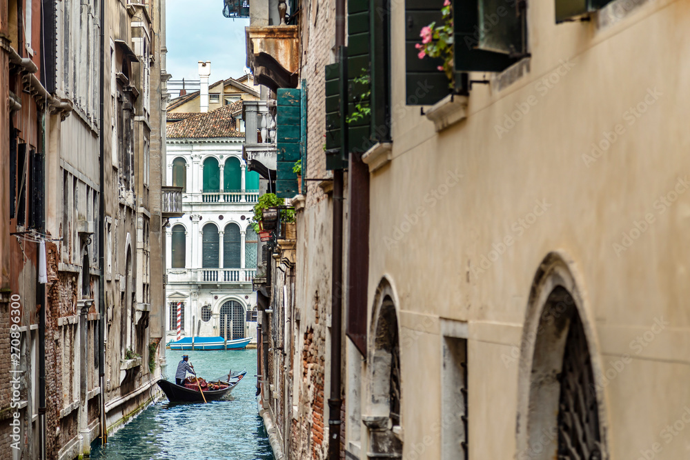 Fototapeta Gondolier w rozebranej kamizelce unoszącej się na gondoli przez wąski kanał wśród przytulnych włoskich domów w Wenecji