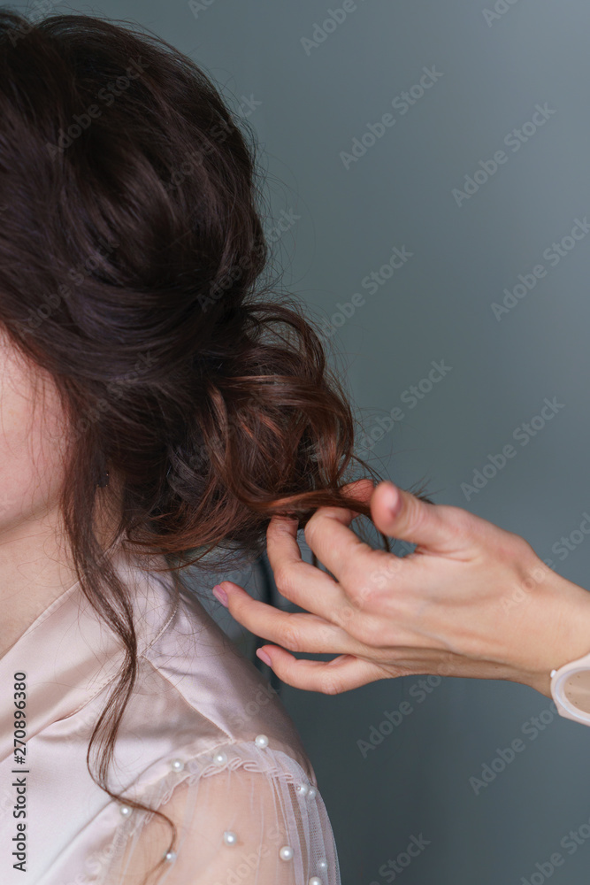 Naklejka premium Hairdresser at work in process of creating wedding hairstyle. Hand hairdresser straightens brown curls. Perfect and beauty in details. Beauty industry