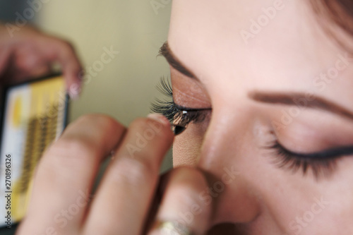 Makeup artist working in makeup studio attaches additional eyelashes to eyes. Close-up of a woman's face. © Vagengeim