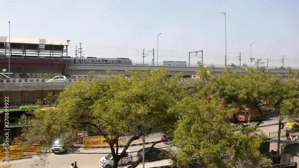 Electric rapid public transport in India, Vehicles moves along delhi metro railroad and passes by Delhi city buildings & skyscrapers, now Indian urban mass transit metro railway system.
