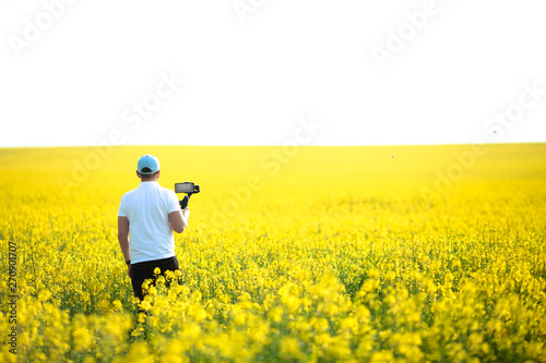 A handsome guy uses a smartphone to take a selfie while sitting in a yellow field of rapeseed.