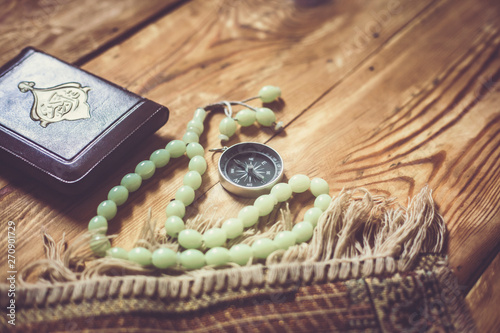 Traditional muslim prayer set bundle. Praying carpet, rosary beads, little version of the Holy Quran and qibla compass on wooden background. Free Space photo