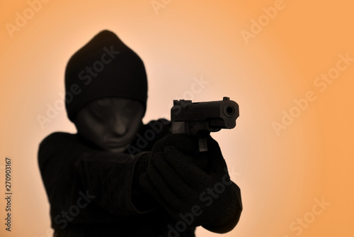Female robber with black gloves and tights over her head holding a gun and aiming. Selective focus. 