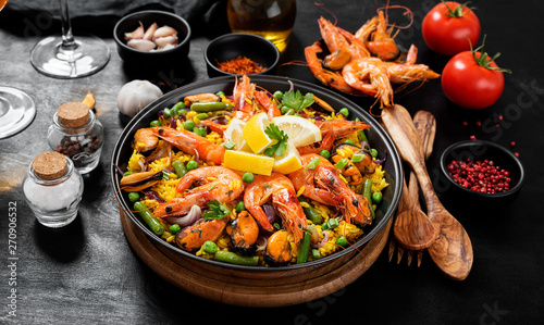 Traditional spanish seafood paella in the fry pan on a black wooden  table.