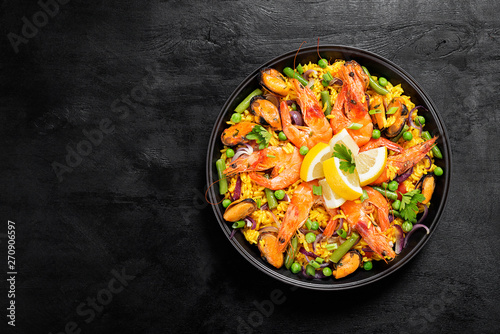 Traditional spanish seafood paella in the fry pan on a black wooden table, top view.
