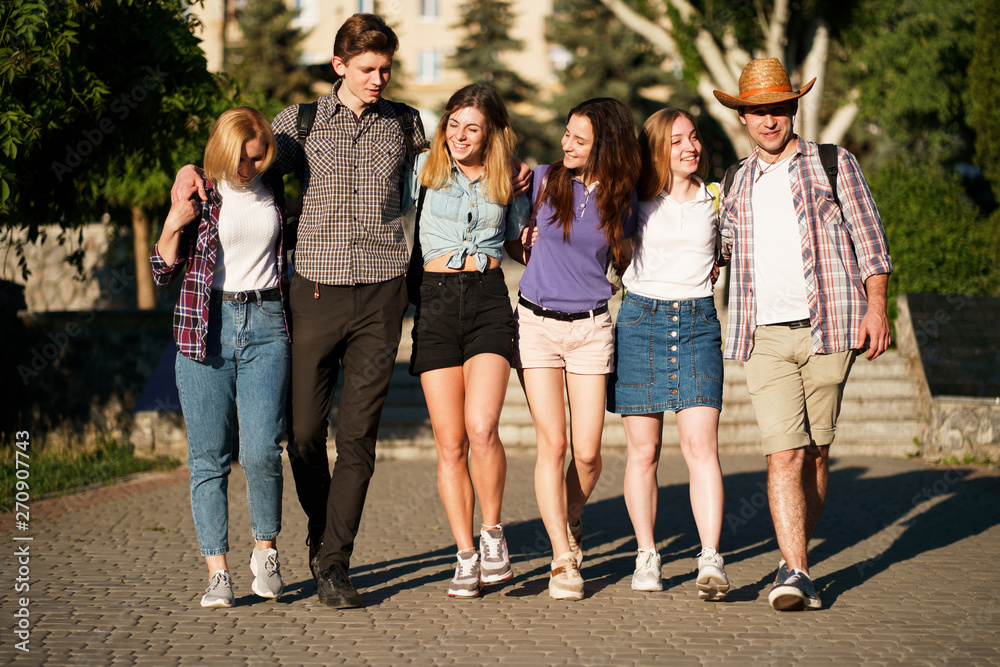 Obraz premium Friendship, togetherness, traveling, vacation, holidays, sightseeing, city tour, student exchange program. Group of young people with backpacks hugging walking in the city
