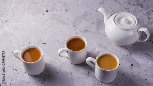 White teapot and white cups of tea or coffee on a gray table