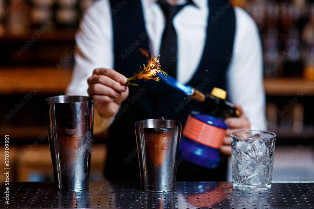 elegant young male bartender preparing a delicious cocktail at the bar. barman szmat razmarin gas torch