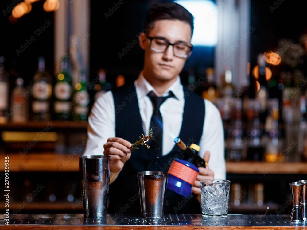 elegant young male barman prepares a delicious cocktail at the bar